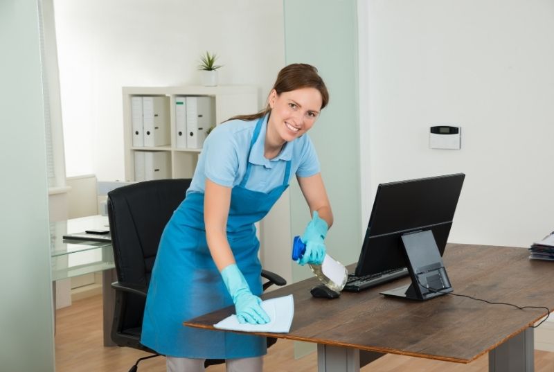 Maid cleaning an office desk with a wipe