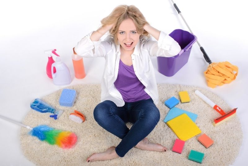 Frustrated Woman holding her head surrounded by cleaning products