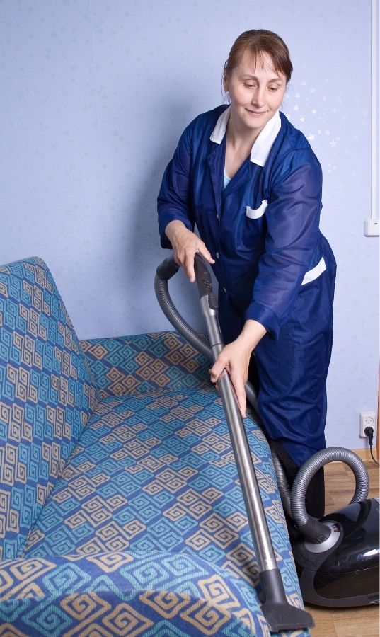 Cleaner vacuuming a fabric couch for a house cleaning services