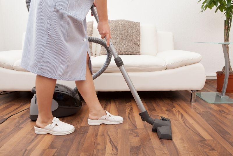 Maid vacuuming a wooden floor in a residential house