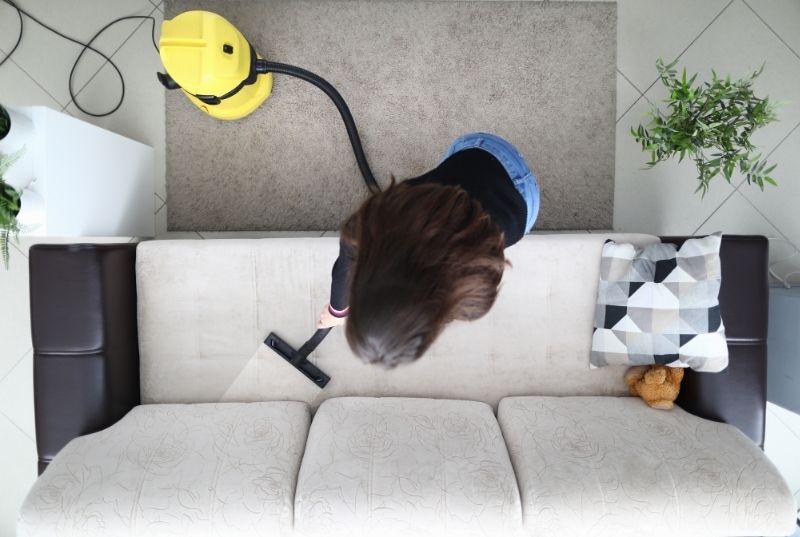 Picture taken from the ceiling of a cleaner vacuuming a couch in an end of lease cleaning services
