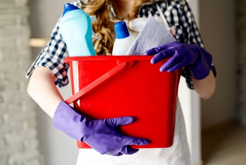 Woman using globes holding a red bucket fill with cleaning products