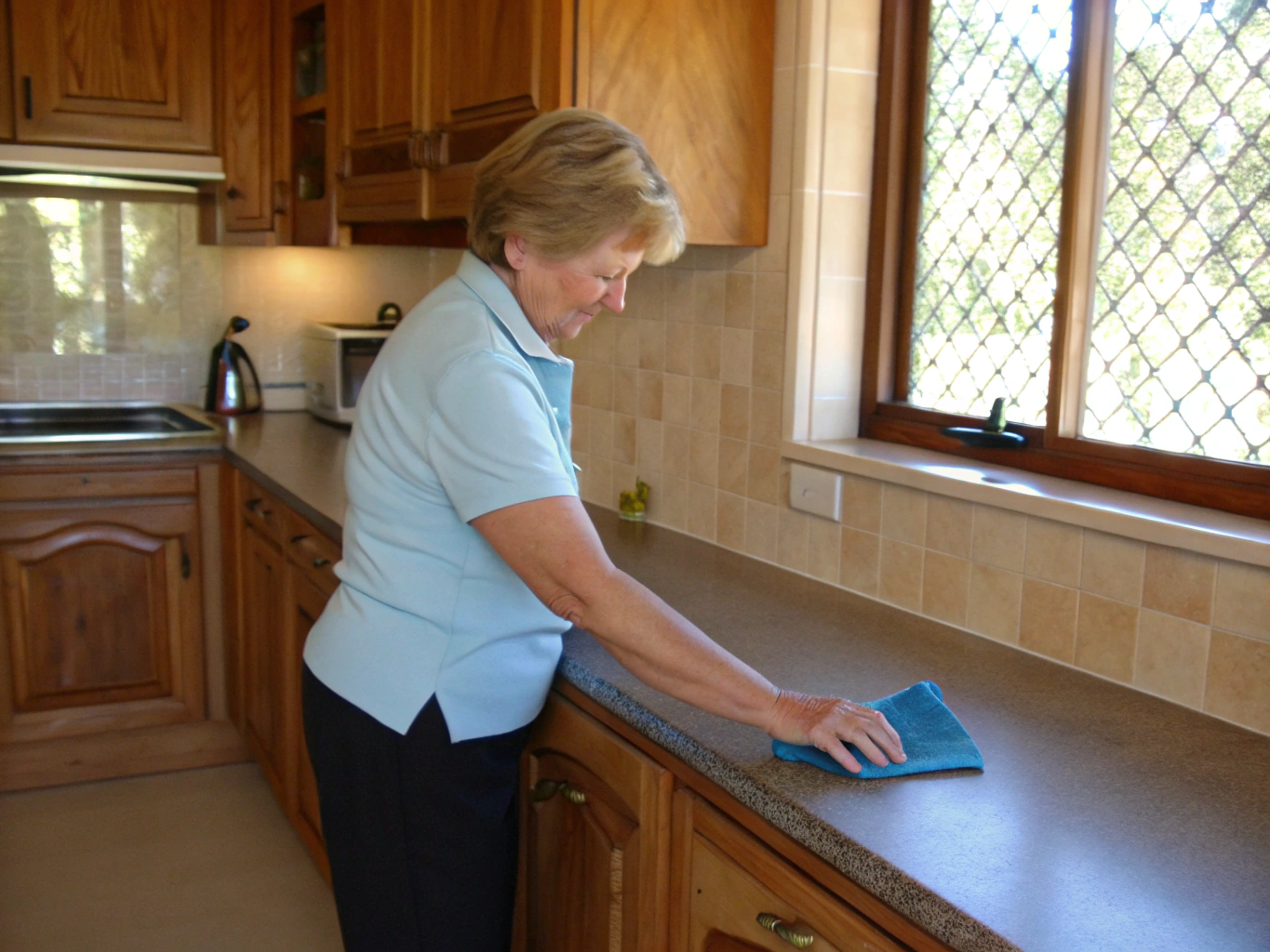 Cleaner wiping a kitchen benchtop in an established Newcastle home for a DVA client
