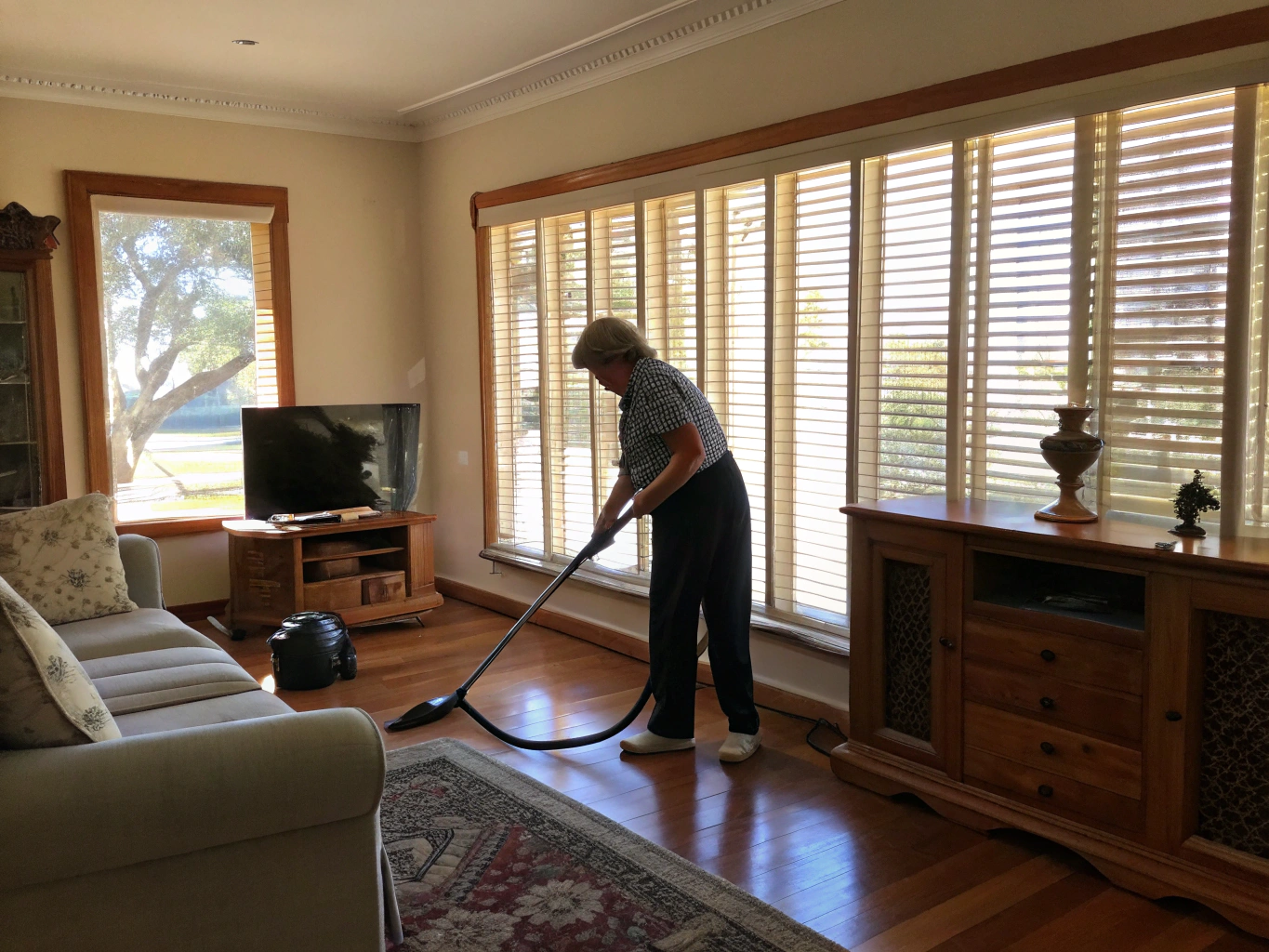 Cleaner vacuuming a living room in an established Newcastle home for a DVA client
